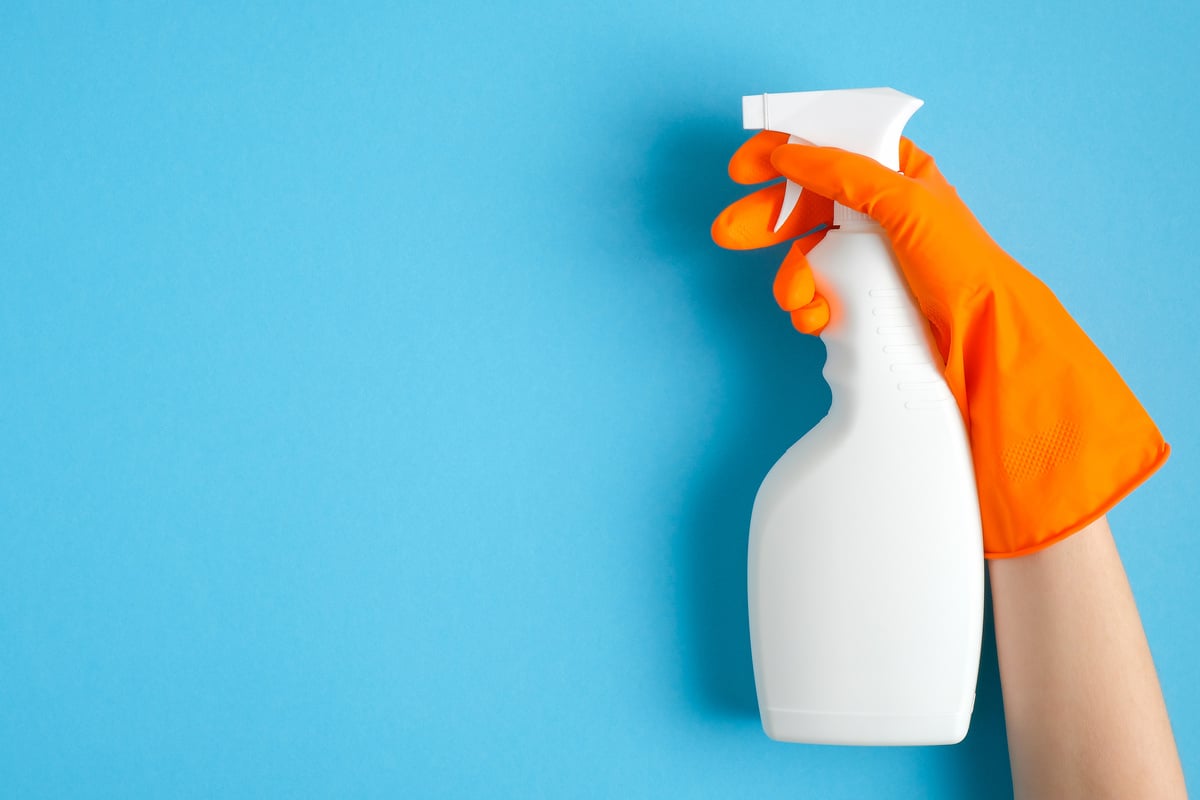 Hand Wearing Orange Glove Holding Disinfectant Spray on Blue Background